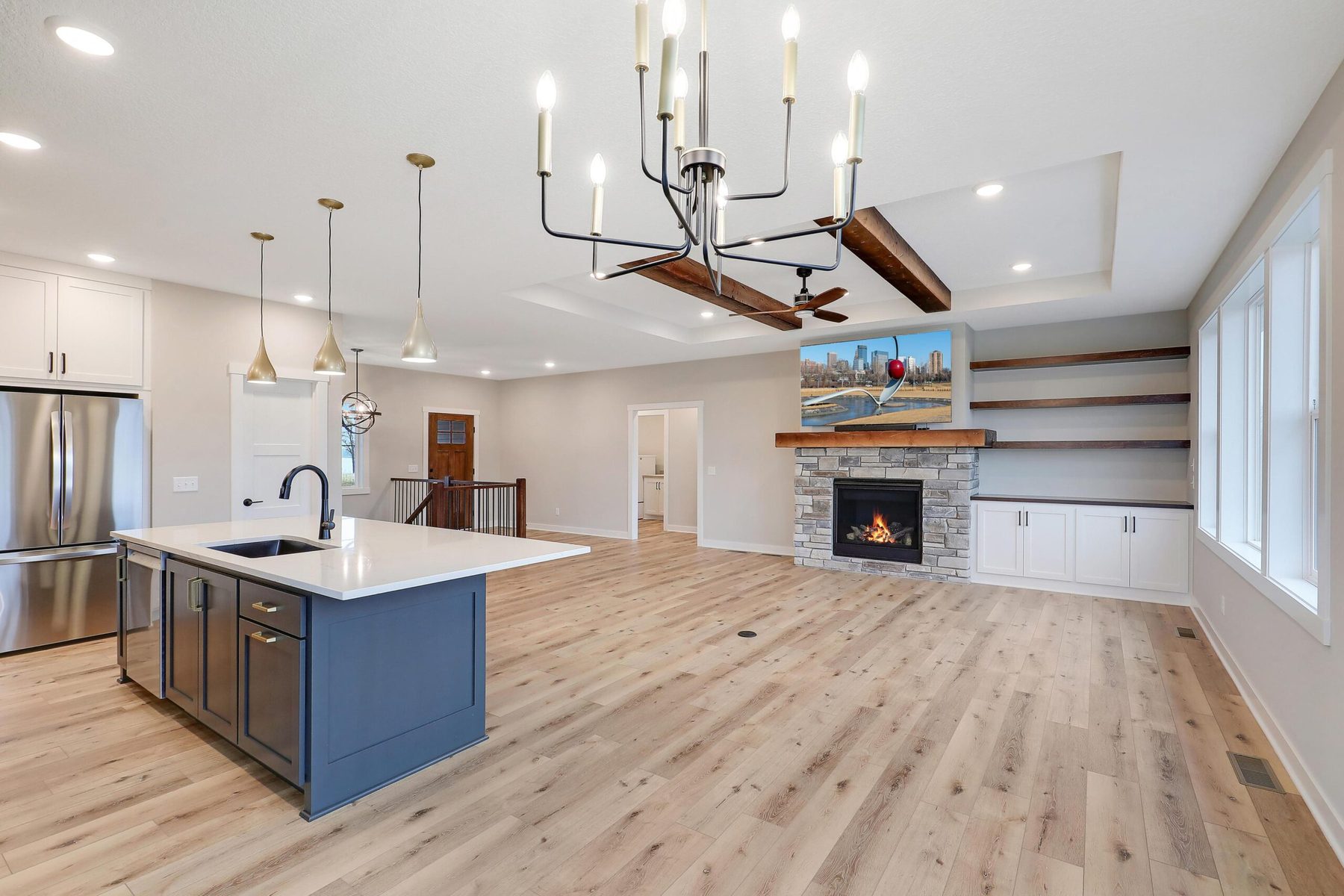 Great room with blue island, stone fireplace and skyline artwork — The Trilogy