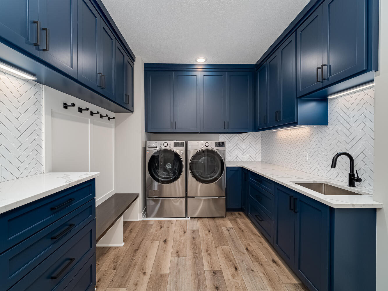Navy-blue mudroom and laundry with herringbone tile and built-in bench
